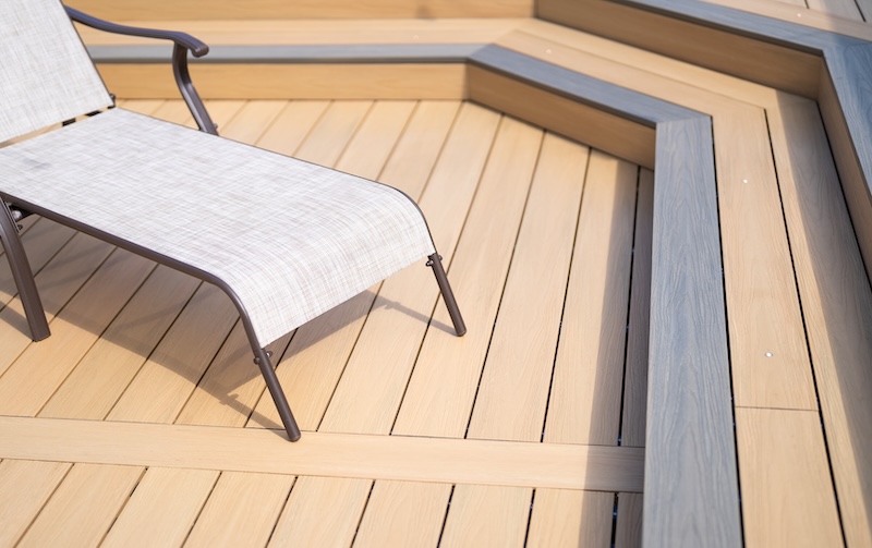 Light brown and grey composite decking in a chevron pattern with sun lounger