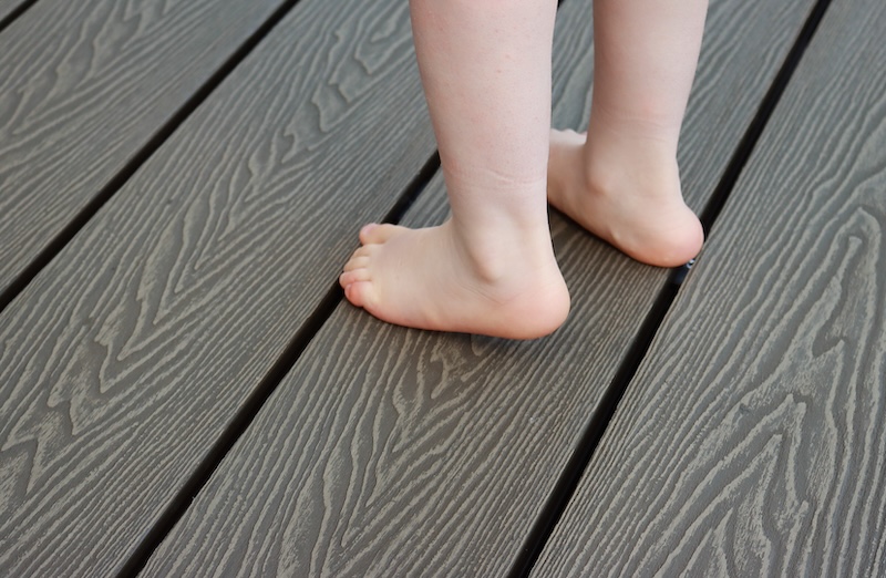 Child’s bare feet standing on woodgrain textured composite decking boards