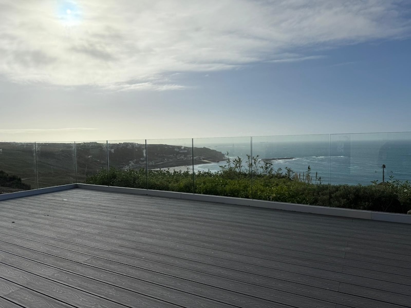 Light grey composite decking terrace with glass balustrade overlooking the sea and coastal landscape