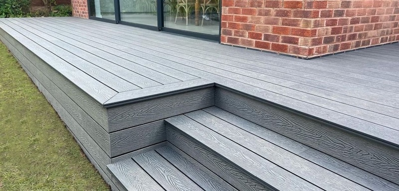 Grey composite decking with built-in steps outside a modern brick home