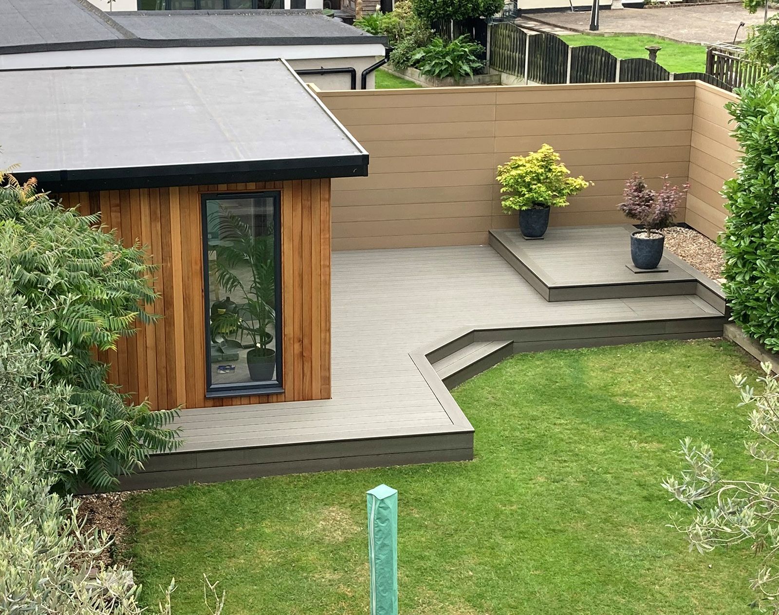 Contemporary garden with beige composite fencing, raised grey decking, and modern planting, providing a low-maintenance and stylish outdoor space.
