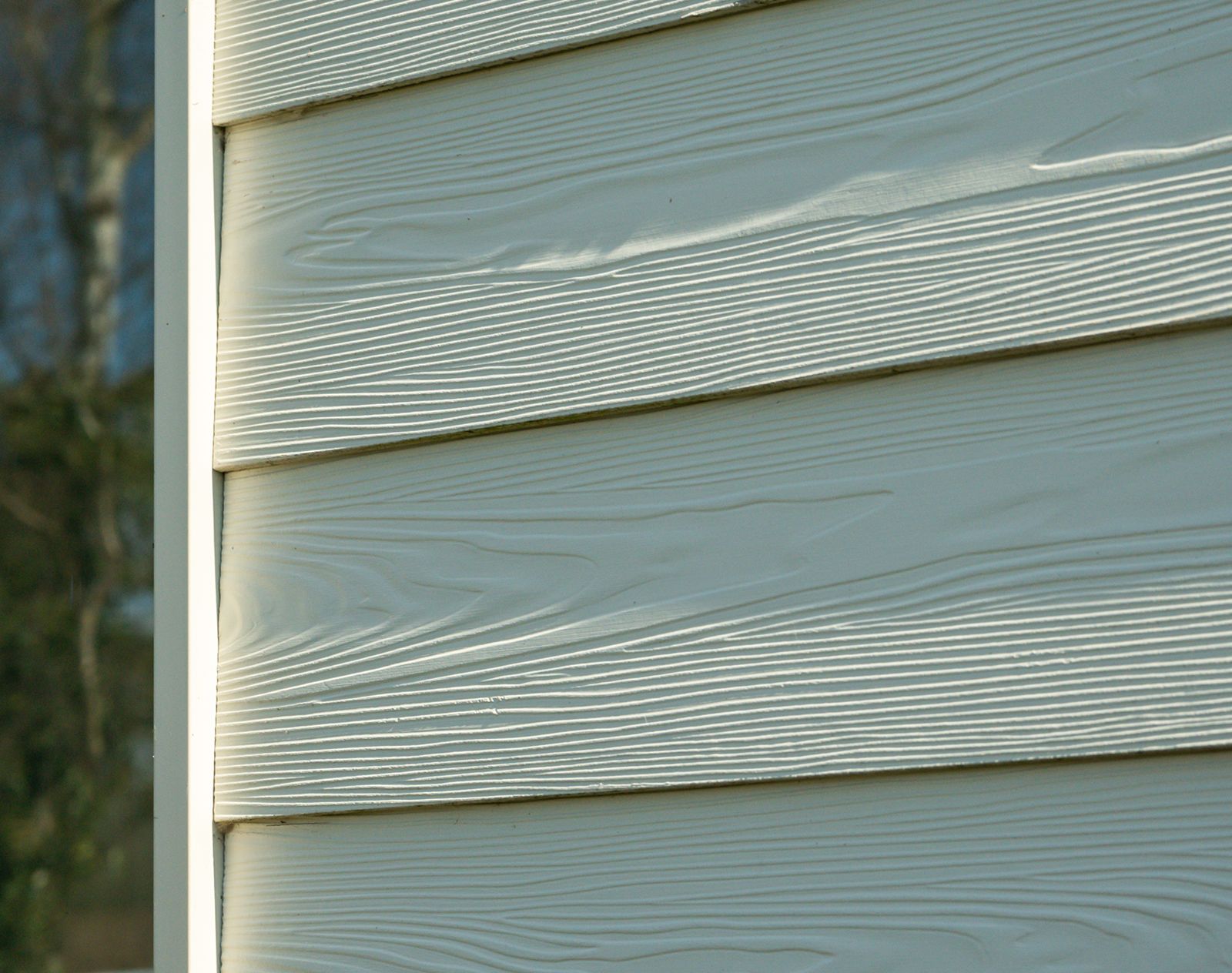 Close-up of white fibre cement cladding boards with realistic woodgrain texture and horizontal overlap installation.