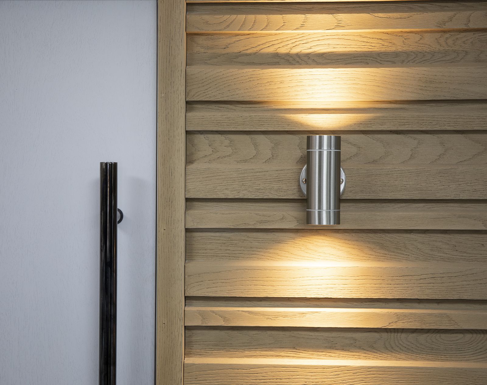 Close-up of illuminated Millboard cladding in a wood-effect finish beside a modern front door, showcasing realistic grain texture and low-maintenance design.