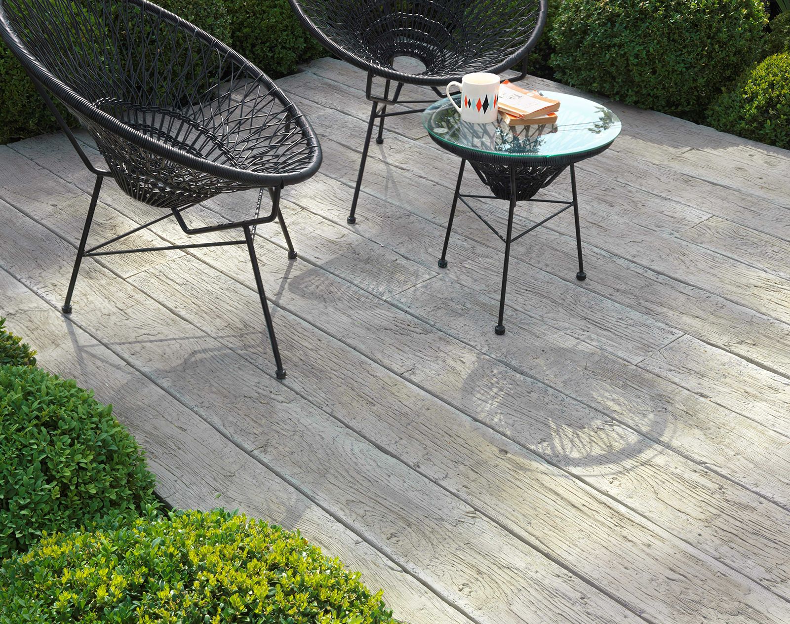 Contemporary outdoor seating on Millboard decking with weathered oak finish, surrounded by neatly clipped green shrubs and modern garden furniture.