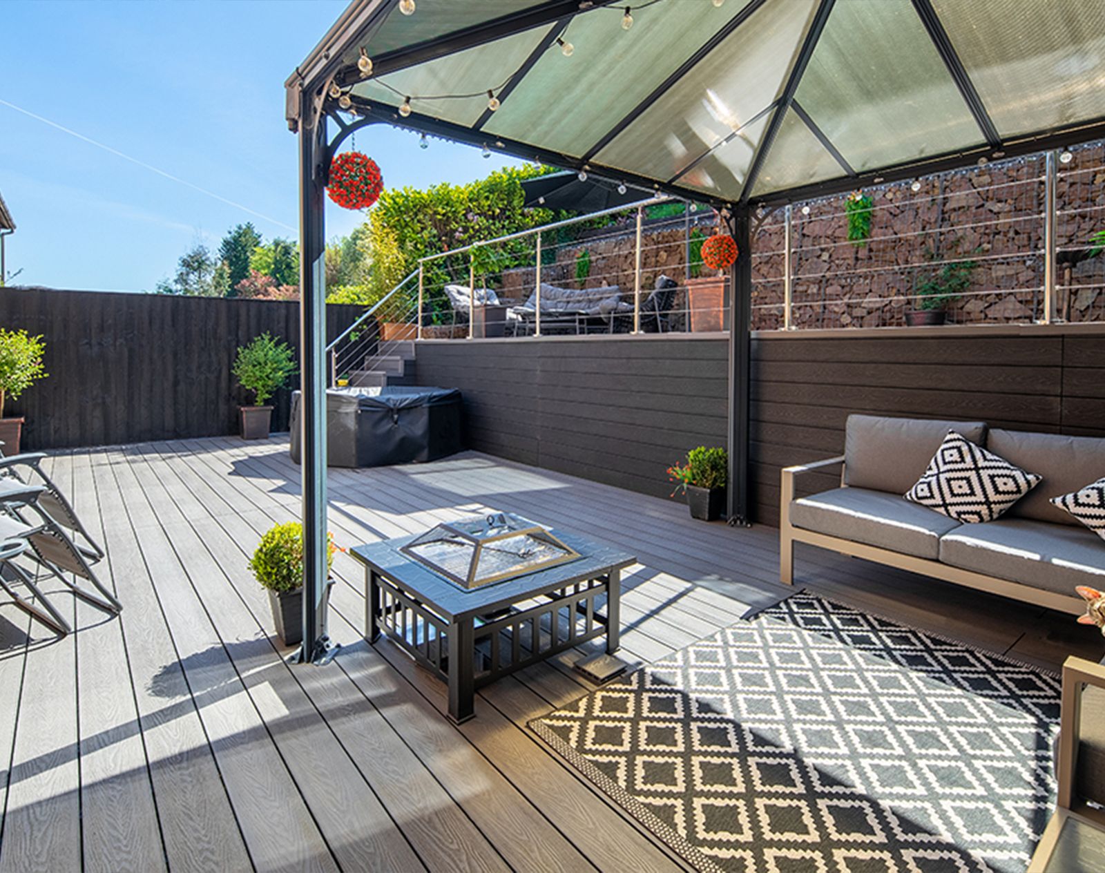 Spacious garden with multi-level composite decking, modern outdoor furniture, and a covered pergola seating area, perfect for stylish low-maintenance outdoor living.