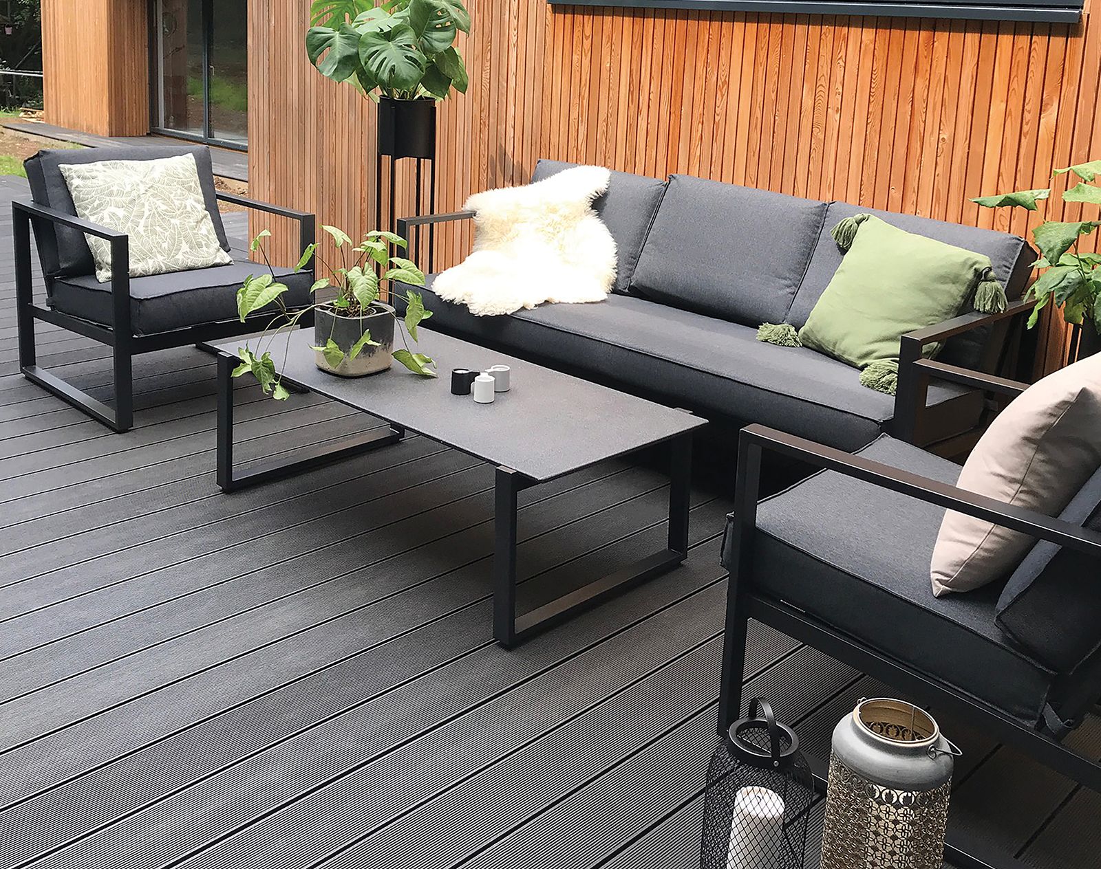 Contemporary outdoor lounge with dark grey composite decking, black metal furniture, and natural timber cladding for a modern garden design.