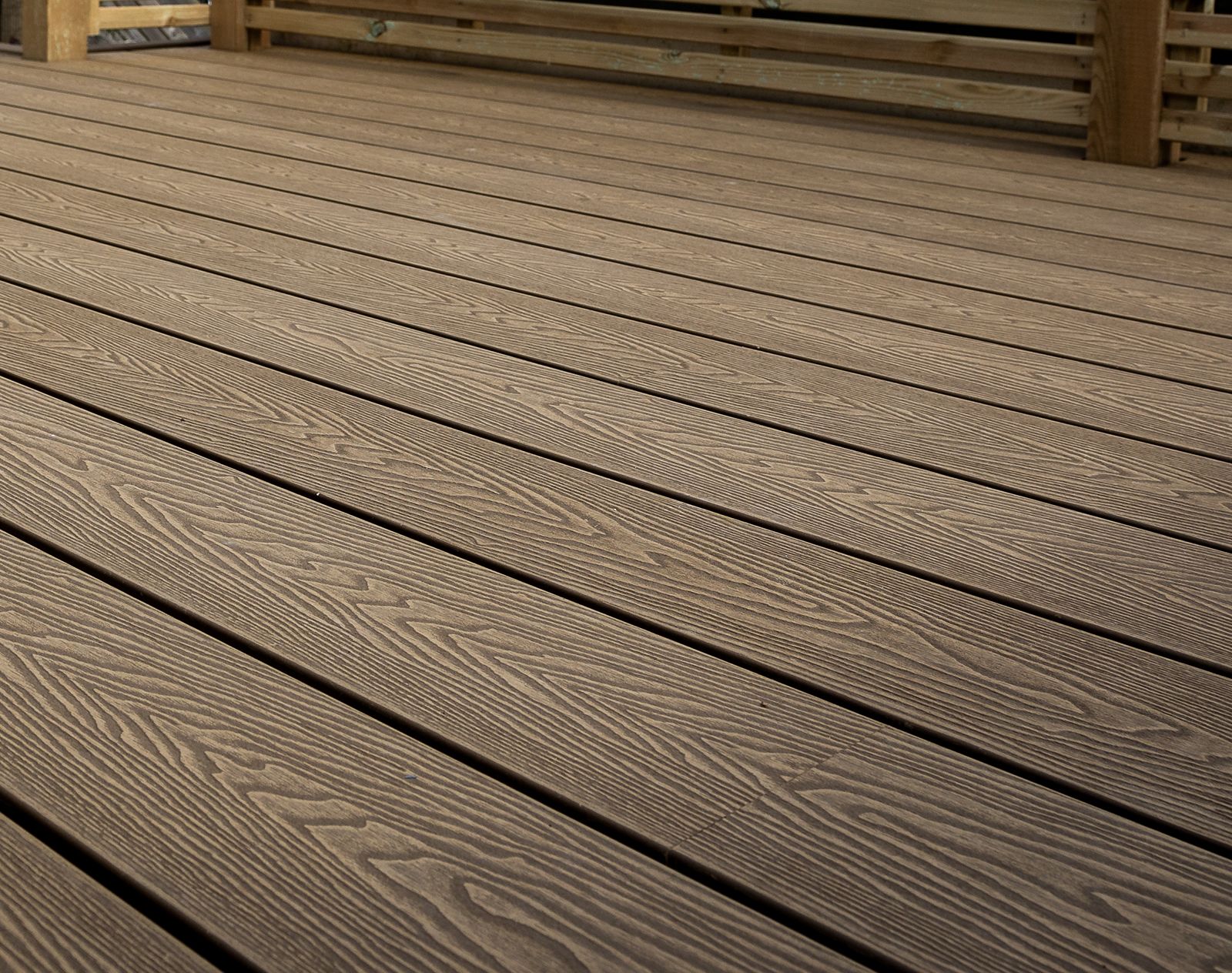 Close-up view of brown woodgrain-effect composite decking boards with realistic textured finish and clean grooved lines.