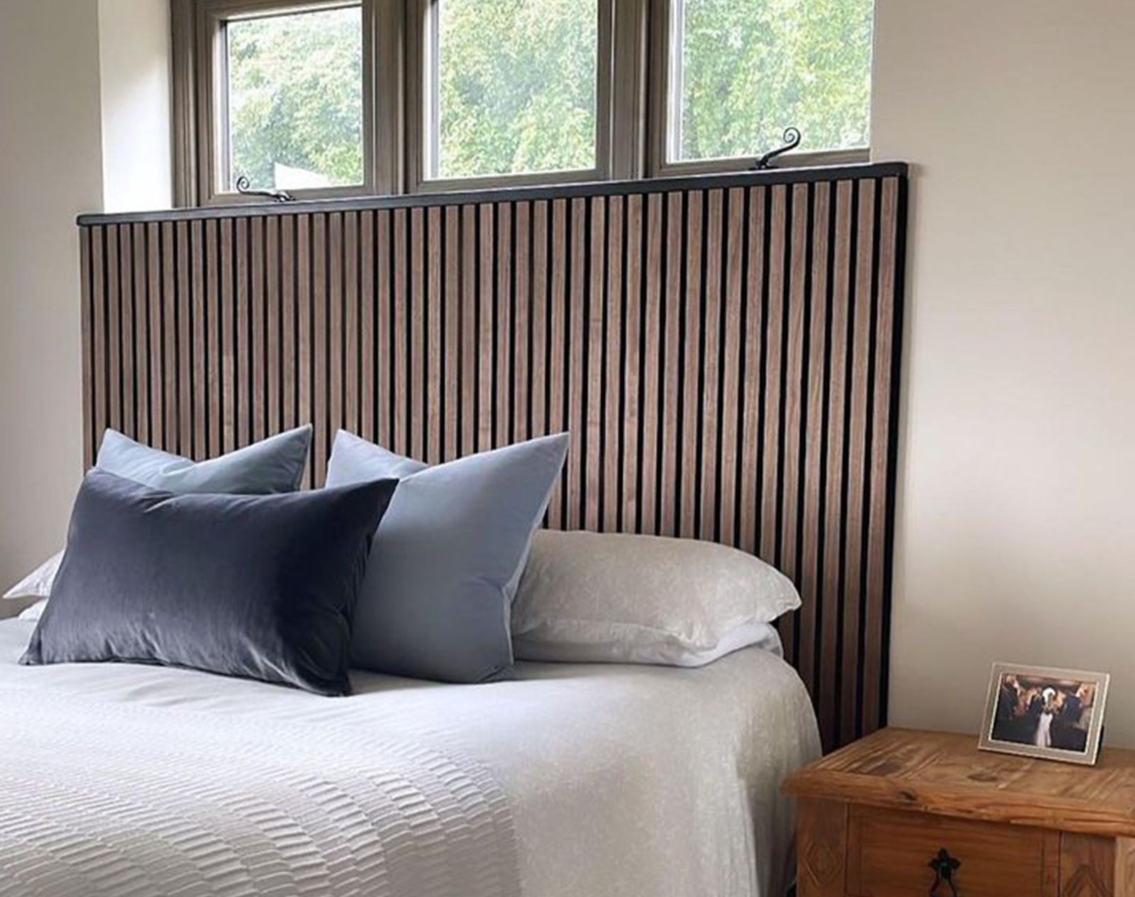 Modern bedroom featuring vertical slat wood wall panelling behind a bed with white bedding and navy cushions, adding texture and style to the space.