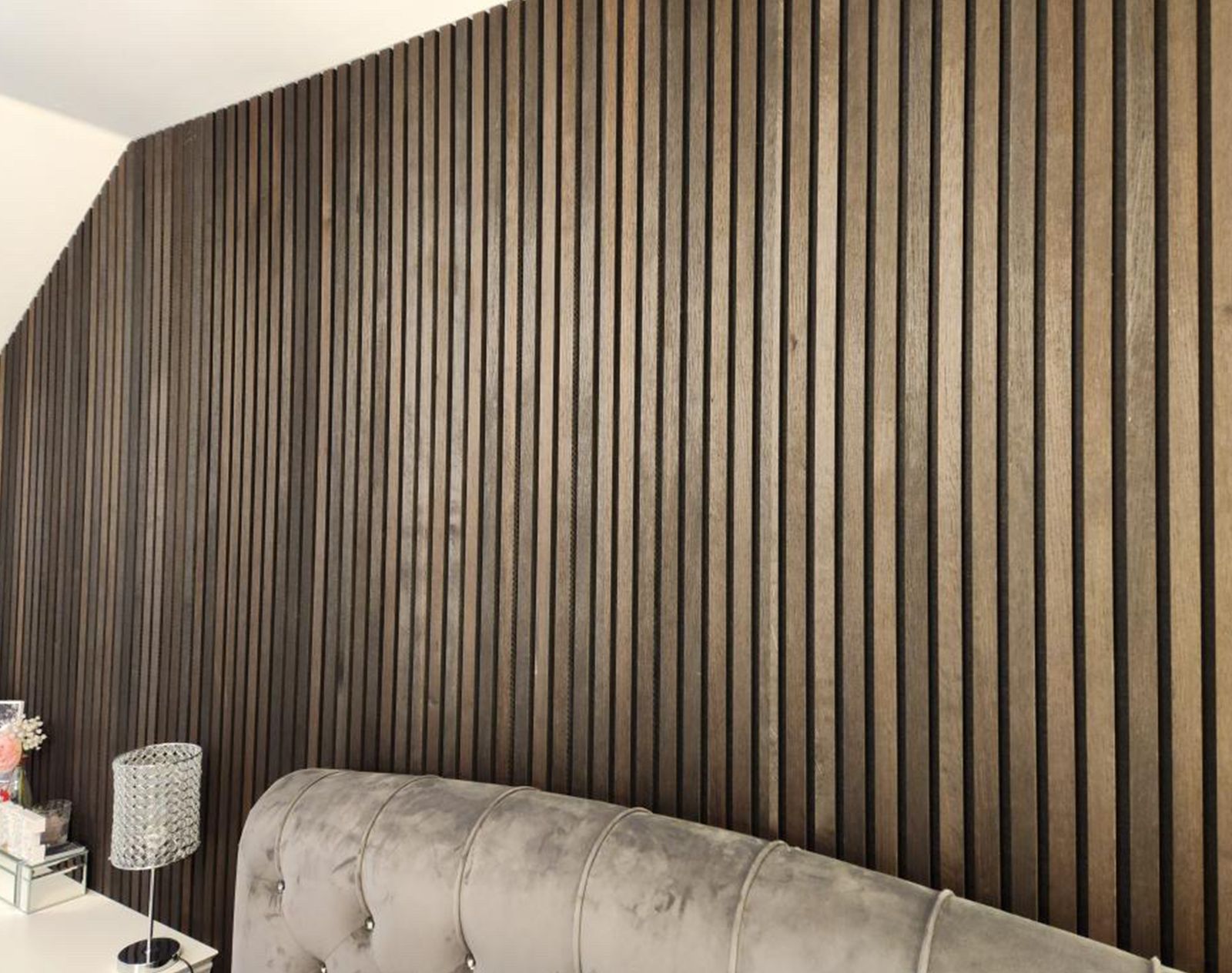 Dark wood slatted wall panelling creating a modern feature wall in a stylish bedroom with a tufted velvet headboard.