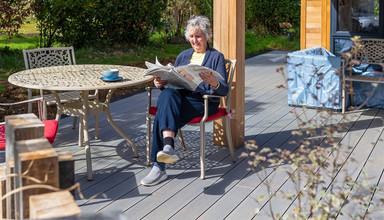 Woman enjoying tea on garden chair atop Cladco Composite Decking at Palstone Lodges