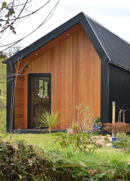 A large garden room with corrugated steel cladding in black and timber slats