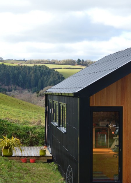 A garden room with steel roofing and cladding sheets overlooking the countryside.