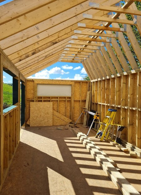 Timber rafters and cross beams show the construction of a large garden room in the countryside.