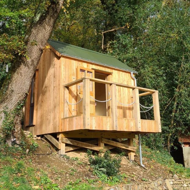 A small wooden recording studio on stilts in the woods with a Juniper Green Corrugated Roof.