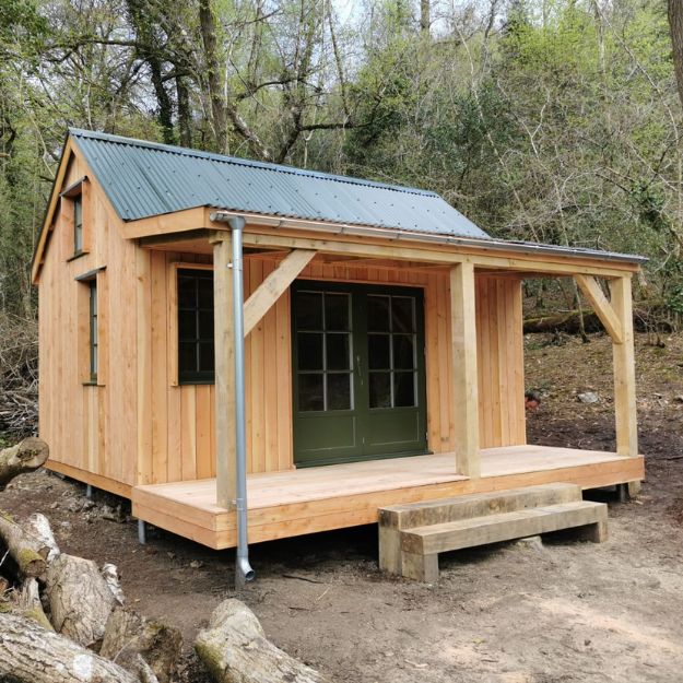 A small wooden cabin in the woods, with double doors at the entrance and a Juniper Green Corrugated Roof.