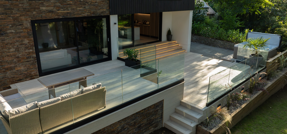 Cornish modern home with Millboard® limed oak decking, glass balustrade, and illuminated garden steps for outdoor entertaining