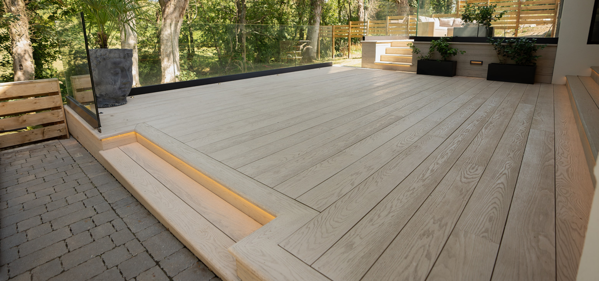Millboard® limed oak decking blending with mature trees in landscaped Cornish garden design