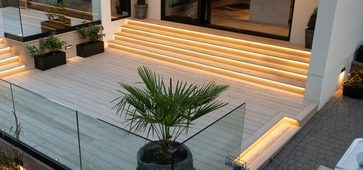 Evening garden view of Millboard® limed oak decking with LED lighting and decorative palm planter
