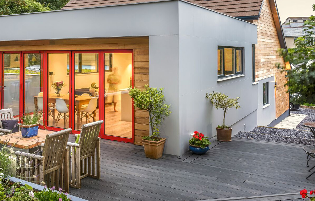 Modern stone grey composite decking outside a contemporary home extension with wooden chairs and potted plants.