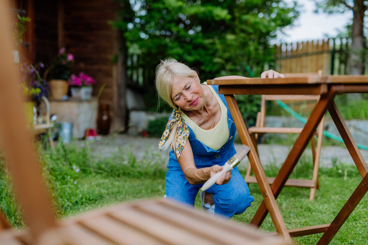 Lady treating wooden garden furniture with wood stain.