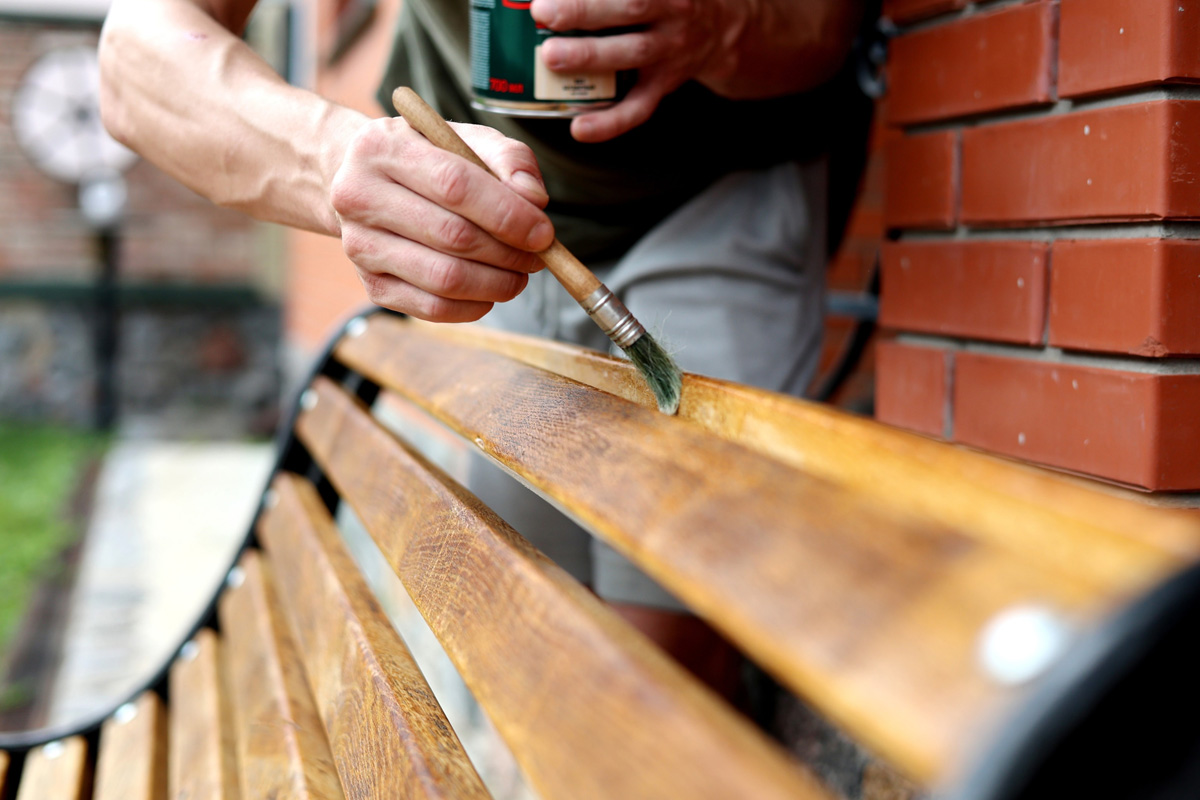 A wooden bench being treated with wood stain.