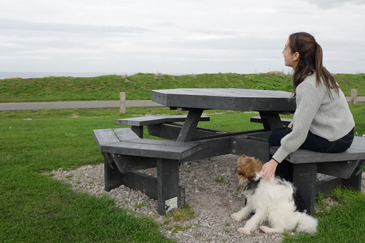 Lady with dog on recycled plastic picnic table in a coastal location.