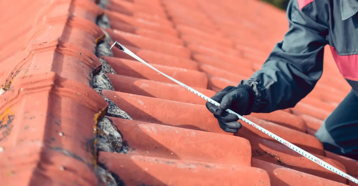 man measuring roof pitch whilst on a roof